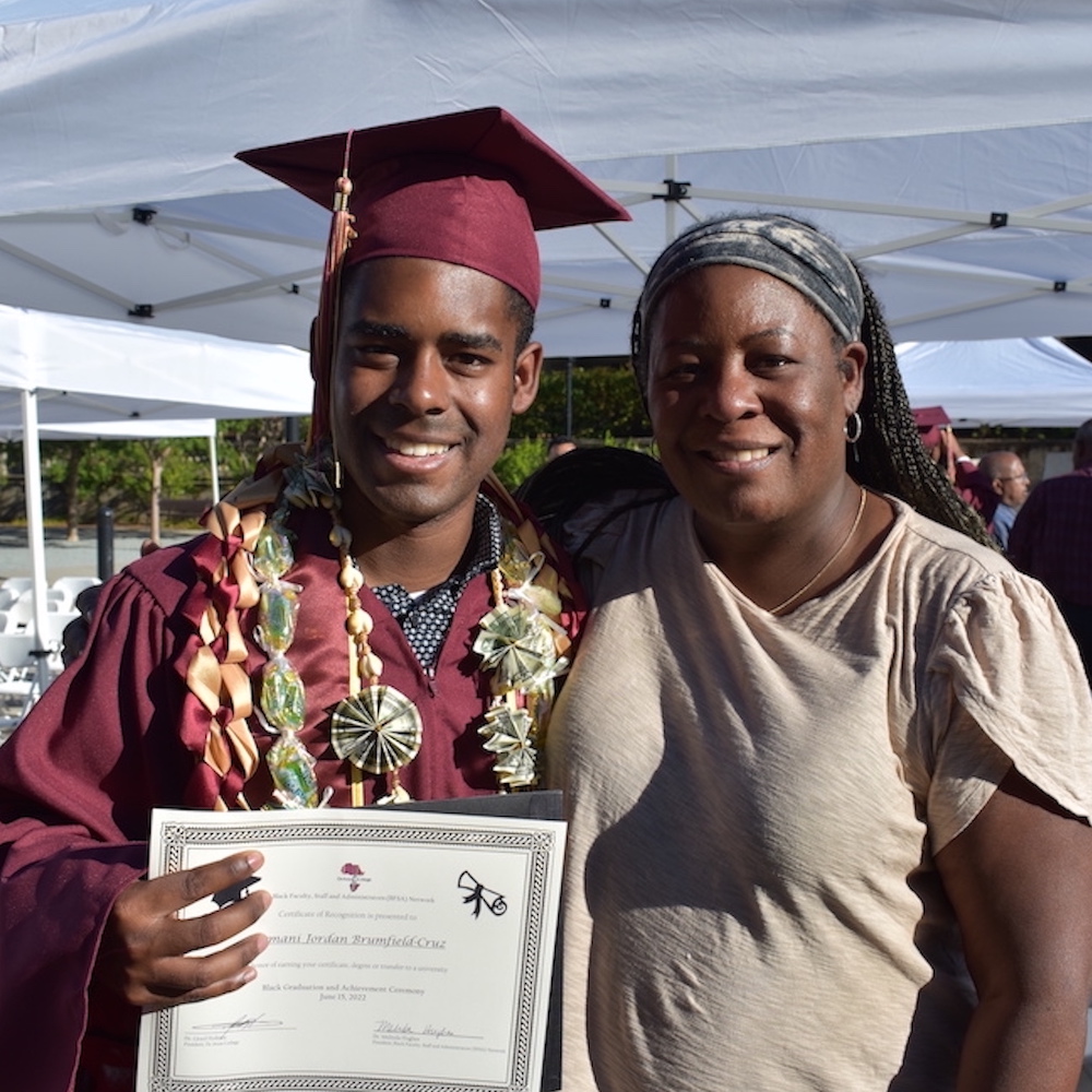 young man in grad cap holding diploma and standing next to woman