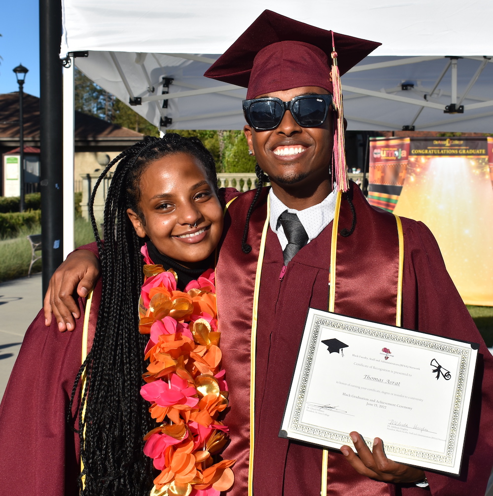smiling young woman with smiling young man in sunglasses, both in grad caps and gowns