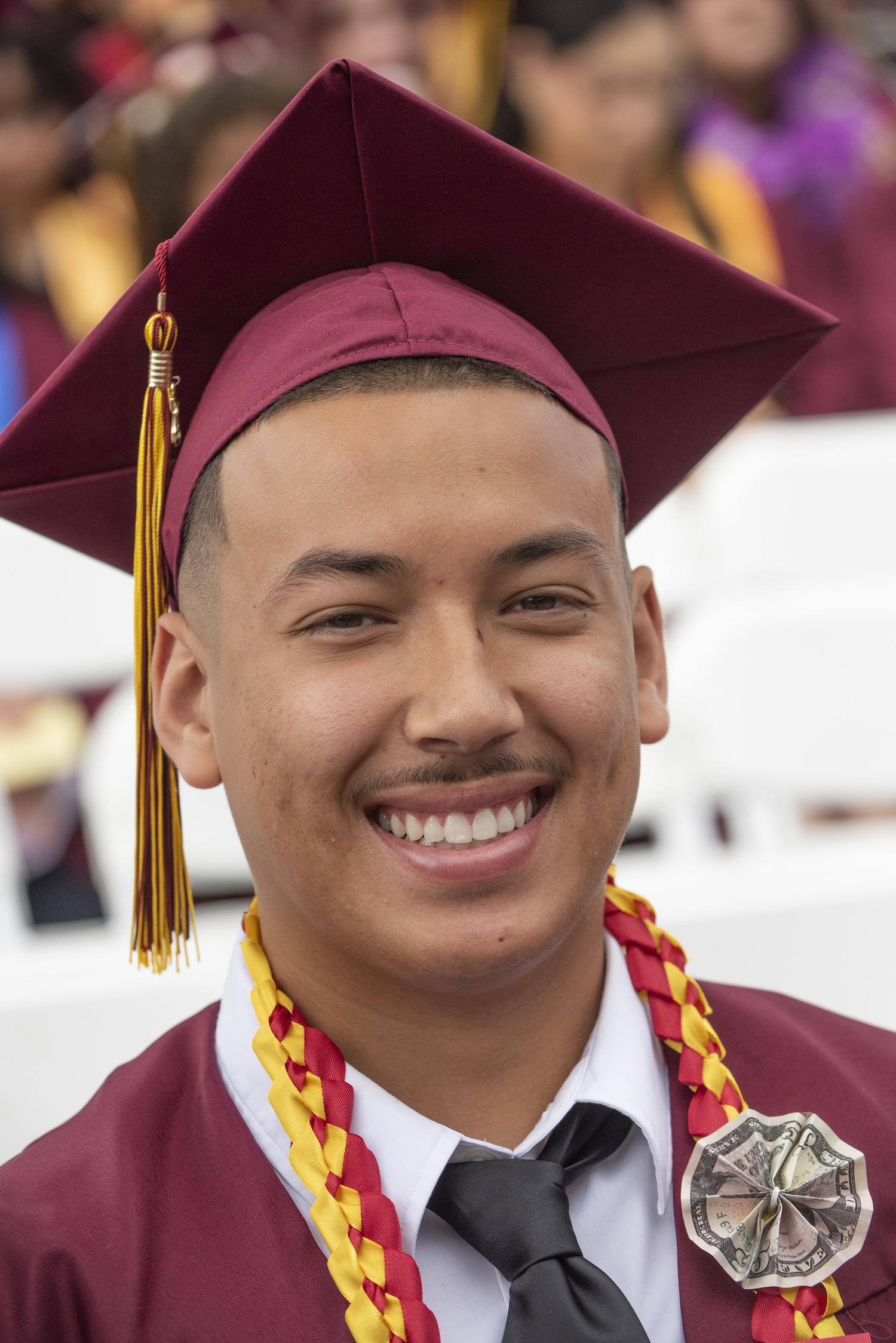 A grad smiles in regalia with a dollar lapel pin