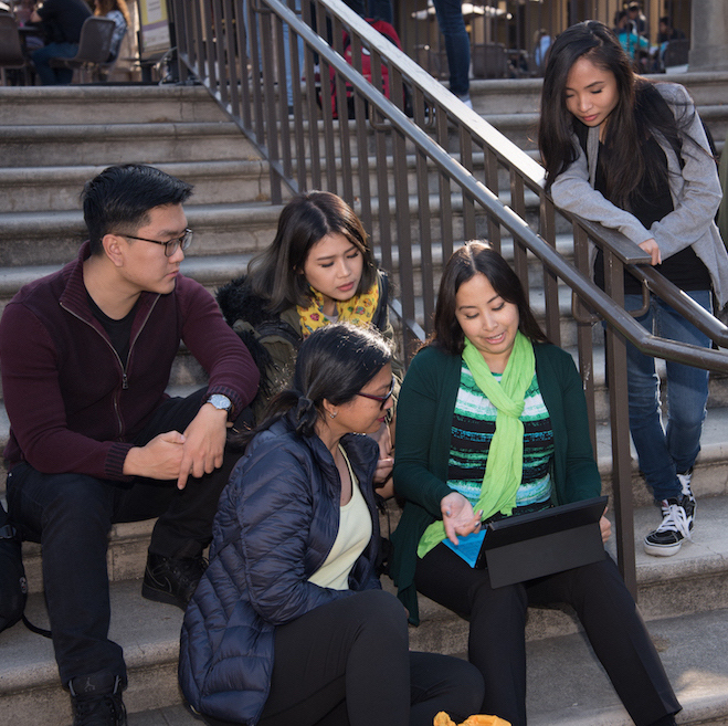 students seated on stone steps looking at computer