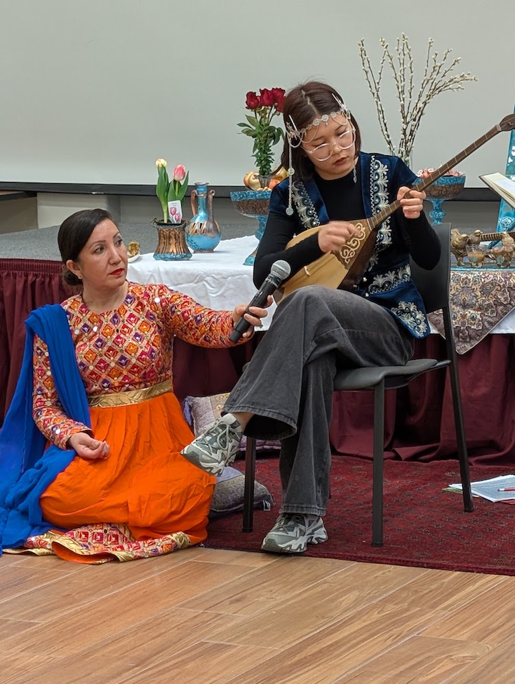 woman holding microphone for another young woman playing stringed instrument