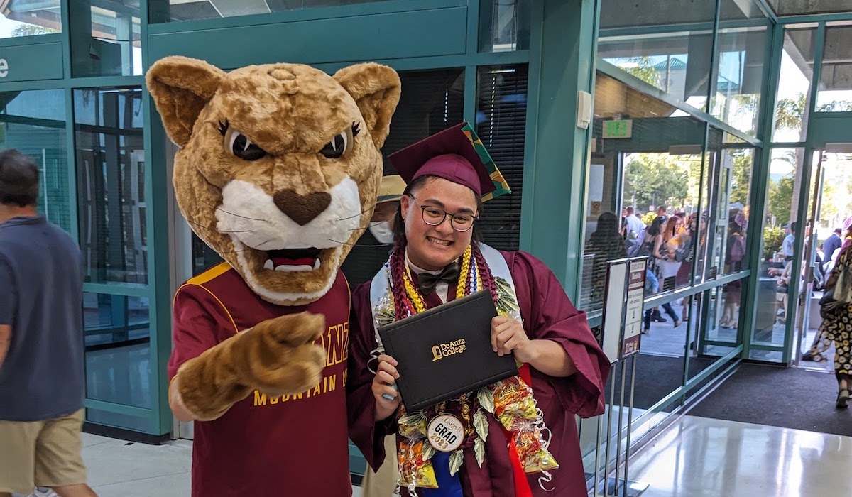 smiling grad holding diploma and leaning against Roary