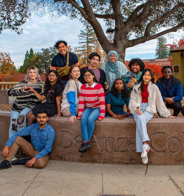 students sitting on wall with De Anza sign
