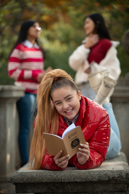 smiling young woman lying flat with notebook