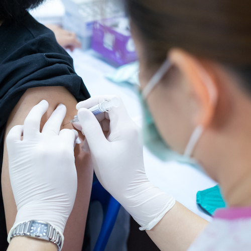 close-up of women in surgical mask administering vaccine to someone's arm