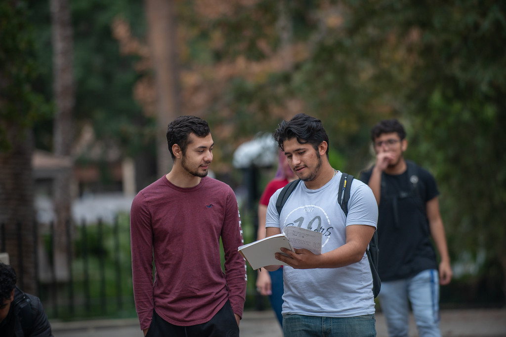 two young men walking and looking at notebook